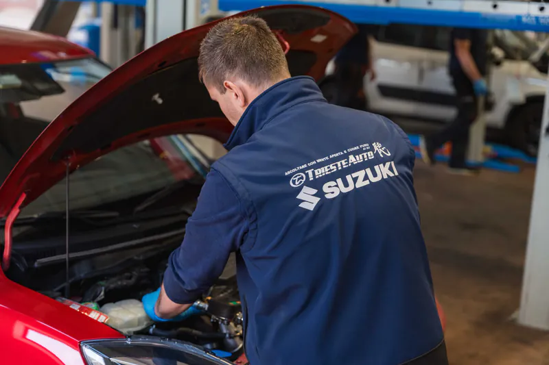 Tecnico Trieste Auto con divisa Suzuki al lavoro sul motore di un'auto nell'officina autorizzata Suzuki di Muggia, Trieste